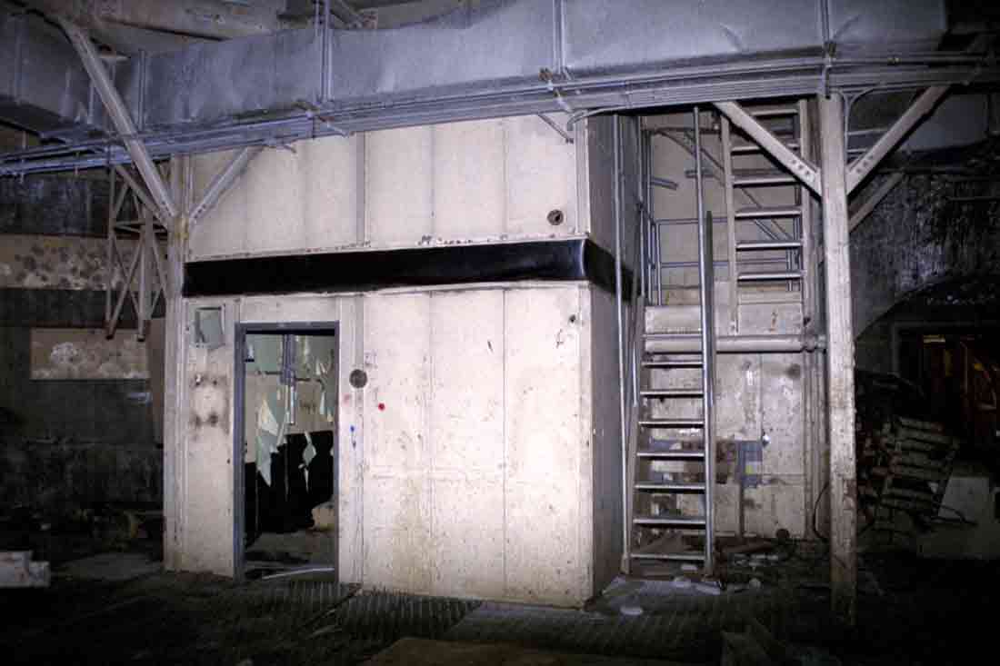 Abandoned industrial room with worn walls and a stairwell.
